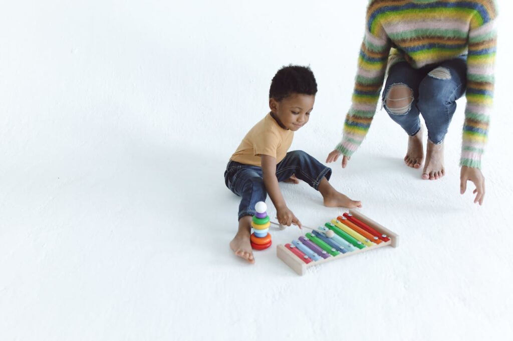 Young child playing with a colorful xylophone indoors, supervised by an adult.